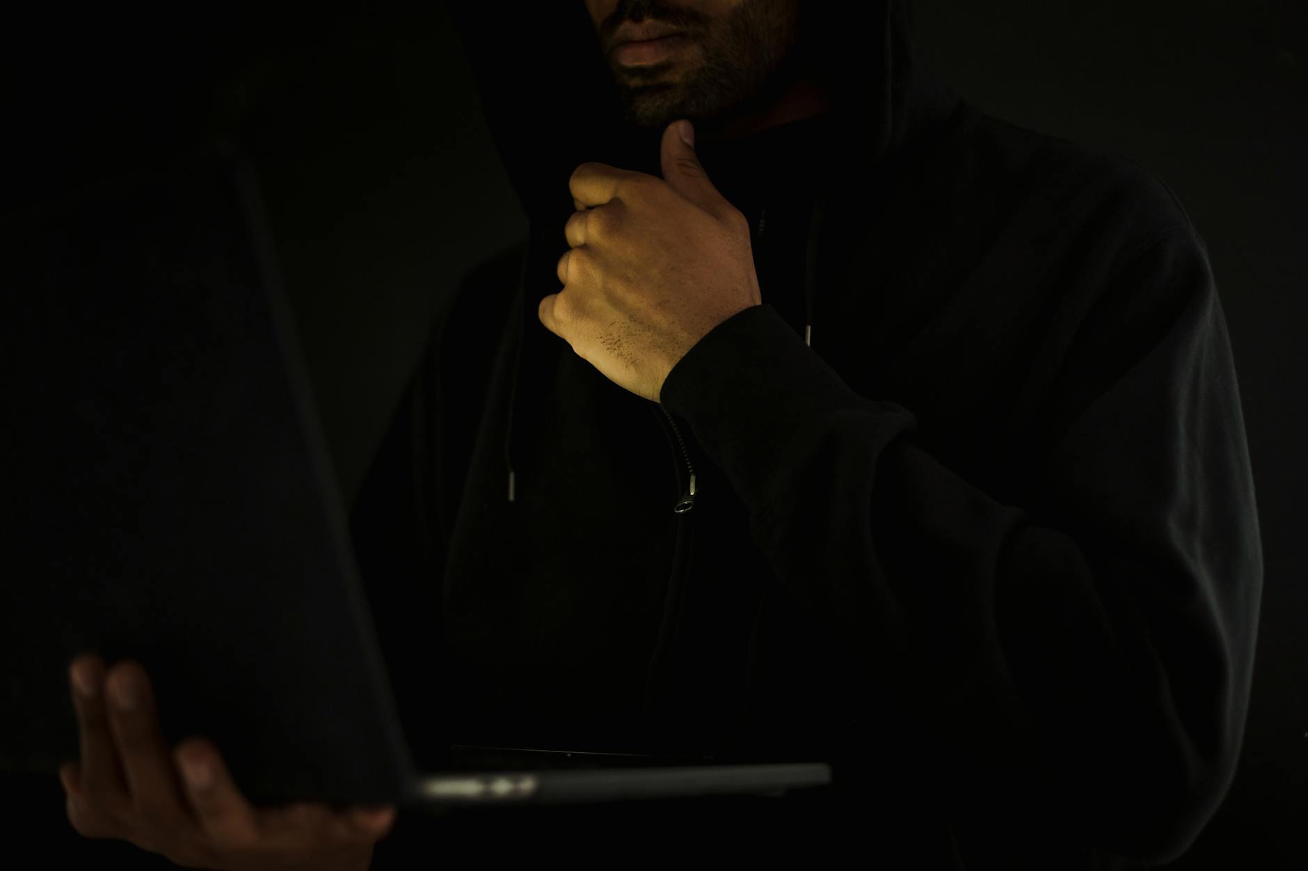 Mężczyzna w kapturze przy laptopie w ciemnym pokoju podczas testów bezpieczeństw