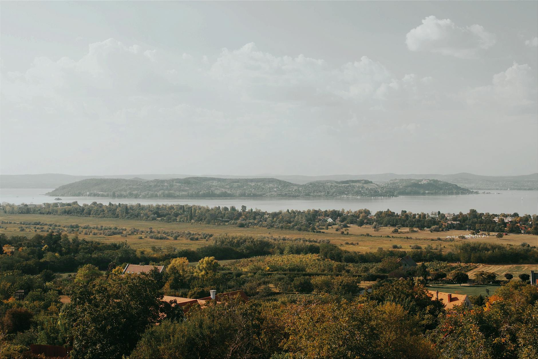 Panorama jeziora Balaton z zielonymi wzgórzami pod pochmurnym niebem