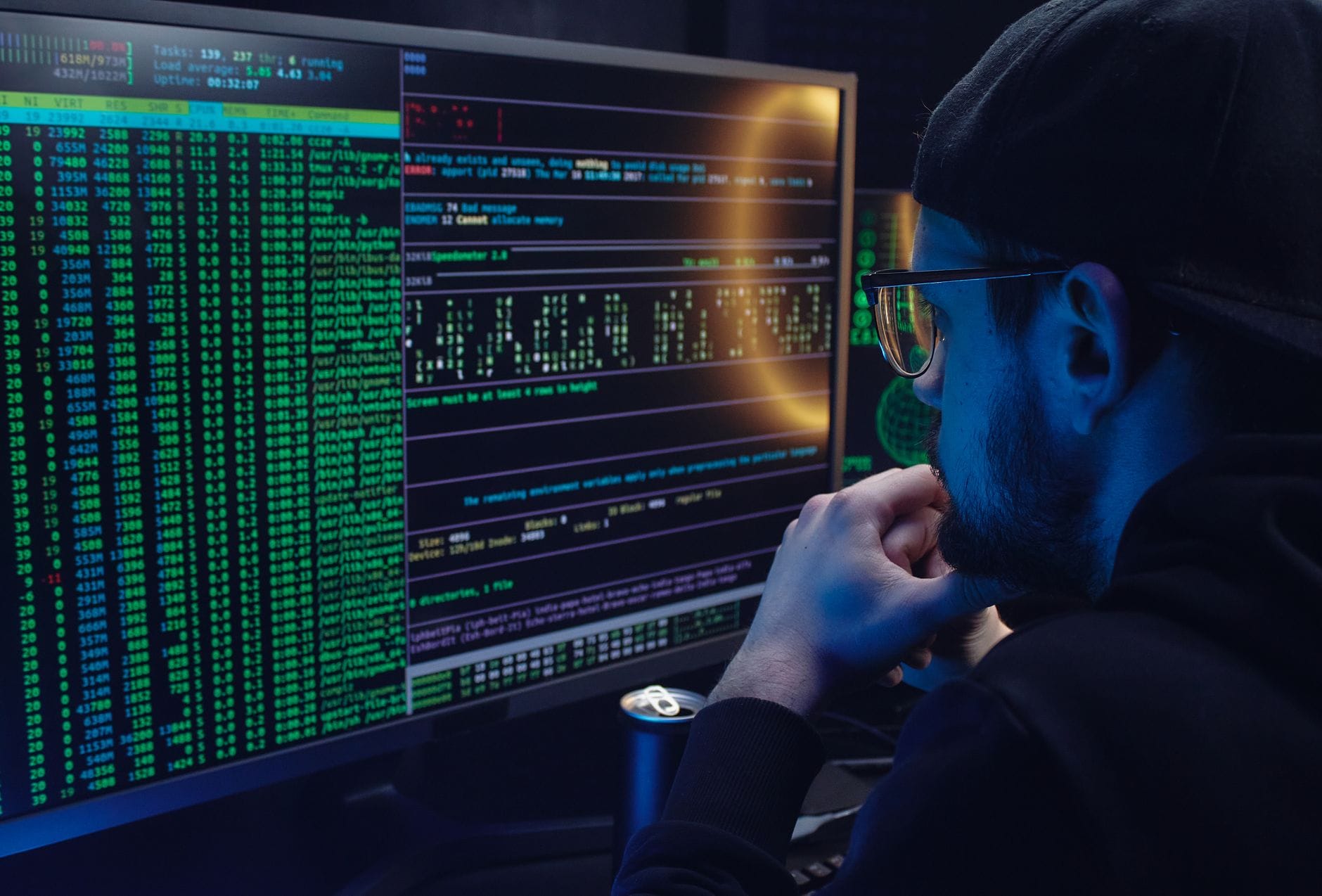 Programista analizuje kod na dwóch monitorach w półmroku